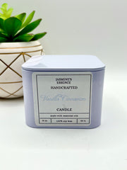 A Vanilla Cinnamon Scented candle with a wooden crackle wick in an 8oz. Pearl white square tin with a label that reads: “Jasmine’s Essence Handcrafted Vanilla Cinnamon Candle”