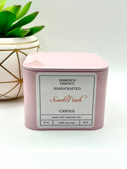 A Sweet Peach Scented candle with a wooden crackle wick in an 8oz. light pink square tin with a label that reads: “Jasmine’s Essence Handcrafted Sweet Peach Candle”