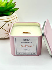 A Sweet Peach Scented candle with a wooden crackle wick in an 8oz. light pink square tin with a label that reads: “Jasmine’s Essence Handcrafted Sweet Peach Candle”