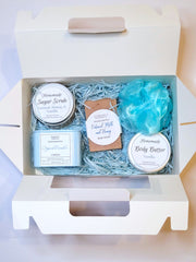 A blue bath set including a handmade soap bar, sugar scrub, body butter, candle, and loofah scented in Vanilla