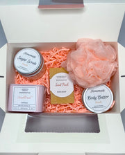 A pink bath set including a handmade soap bar, sugar scrub, body butter, candle, and loofah scented in peach