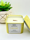 A Citrus Bliss Scented candle with a wooden crackle wick in an 8oz. Yellow square tin with a label that reads: “Jasmine’s Essence Handcrafted Citrus Bliss Candle”