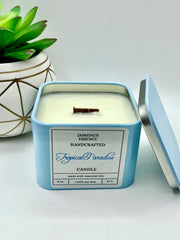 A Tropical Paradise Scented candle with a wooden crackle wick in an 8oz. Light blue square tin with a label that reads: “Jasmine’s Essence Handcrafted Tropical Paradise Candle”