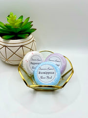 Three shower bombs in a small decorative dish in the scents Eucalyptus , lavender, and peppermint with a label reading: “Jasmine’s Essence Shower Bomb”