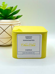 A Citrus Bliss Scented candle with a wooden crackle wick in an 8oz. Yellow square tin with a label that reads: “Jasmine’s Essence Handcrafted Citrus Bliss Candle”