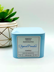 A Tropical Paradise Scented candle with a wooden crackle wick in an 8oz. Light blue square tin with a label that reads: “Jasmine’s Essence Handcrafted Tropical Paradise Candle”